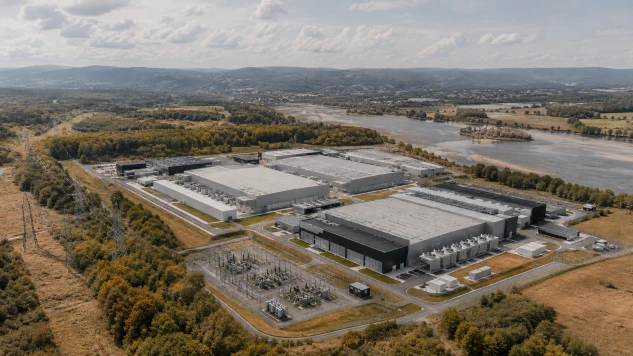 Aerial view of a large data center campus beside a low-flow river, surrounded by power infrastructure and heat-stressed vegetation.